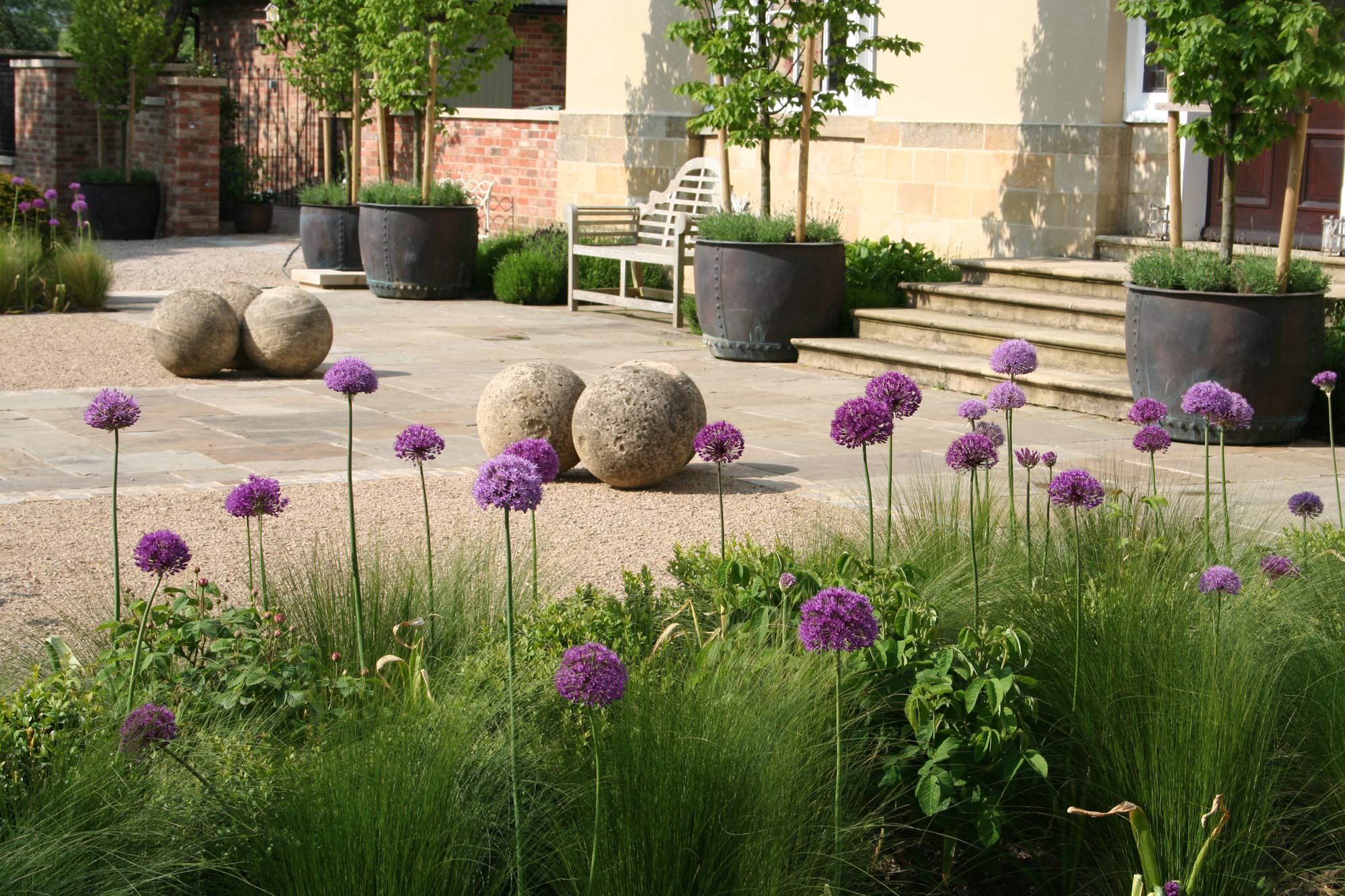 Planted borders including allium flower heads, grasses and roses jostle with stone spheres Design by Peter Eustance